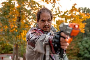 LARP participant in costume aims prop weapon during autumn outdoor roleplay event.