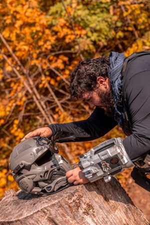 Person wearing dark clothing adjusts mountain bike equipment on a rock with vibrant autumn foliage in background.