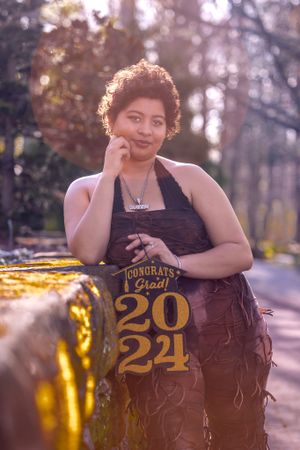 A graduation photo featuring a black dress and 2021 decor captured in warm sunlight with bokeh effects in the background.