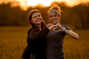 Two people making heart shapes with their hands while posing together at sunset in a golden field.