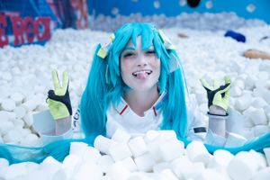 Cosplayer with bright turquoise wig poses playfully in a pit filled with white foam blocks.