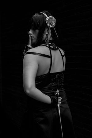 A dramatic black and white portrait shows someone in gothic dress with straps and a decorative floral headpiece from behind.
