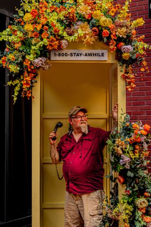 A wooden door with '1-800-STAY-AWHILE' sign adorned by vibrant orange and yellow floral arrangements.