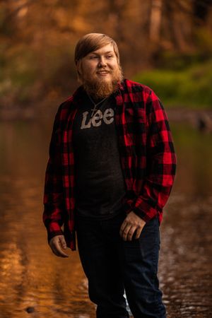Person wearing red and black buffalo plaid flannel and Lee t-shirt stands on wet autumn path at sunset.