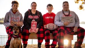 Family group wearing matching buffalo plaid pajama pants poses together with their dog at sunset.