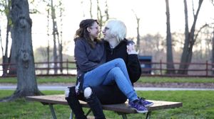 Two people relax on a park bench under bare trees in winter, one drinking from a water bottle.