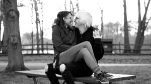 A black and white photo shows two people sitting closely together and sharing a tender moment on a park bench.