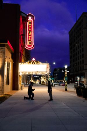 A romantic proposal silhouette under the illuminated Civic Theater sign at night with red neon lights.