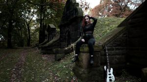 A decorated electric guitar leans against stone steps in a moody autumn forest setting with someone sitting above.