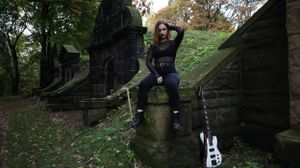 A person poses at a historic stone staircase in a wooded area during autumn.