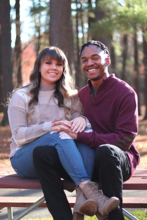 A romantic couple sits together on a park bench in autumn, sharing a joyful moment in casual sweaters and denim.