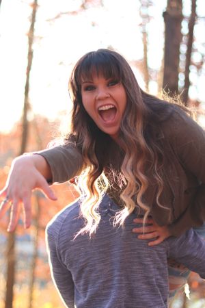 Energetic woman with long wavy hair laughs joyfully while posing outdoors during golden hour sunset.