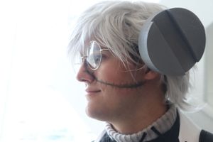 Person with silver hair and sunglasses looking sideways against a light background.