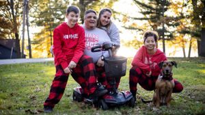 A family group wearing red clothes sits together with their dog in a grassy outdoor setting during sunset.