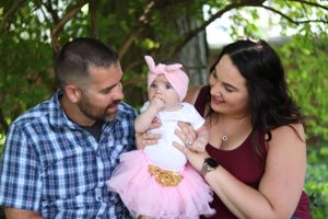 Happy family spending time together outdoors with baby wearing pink tutu dress on sunny day.