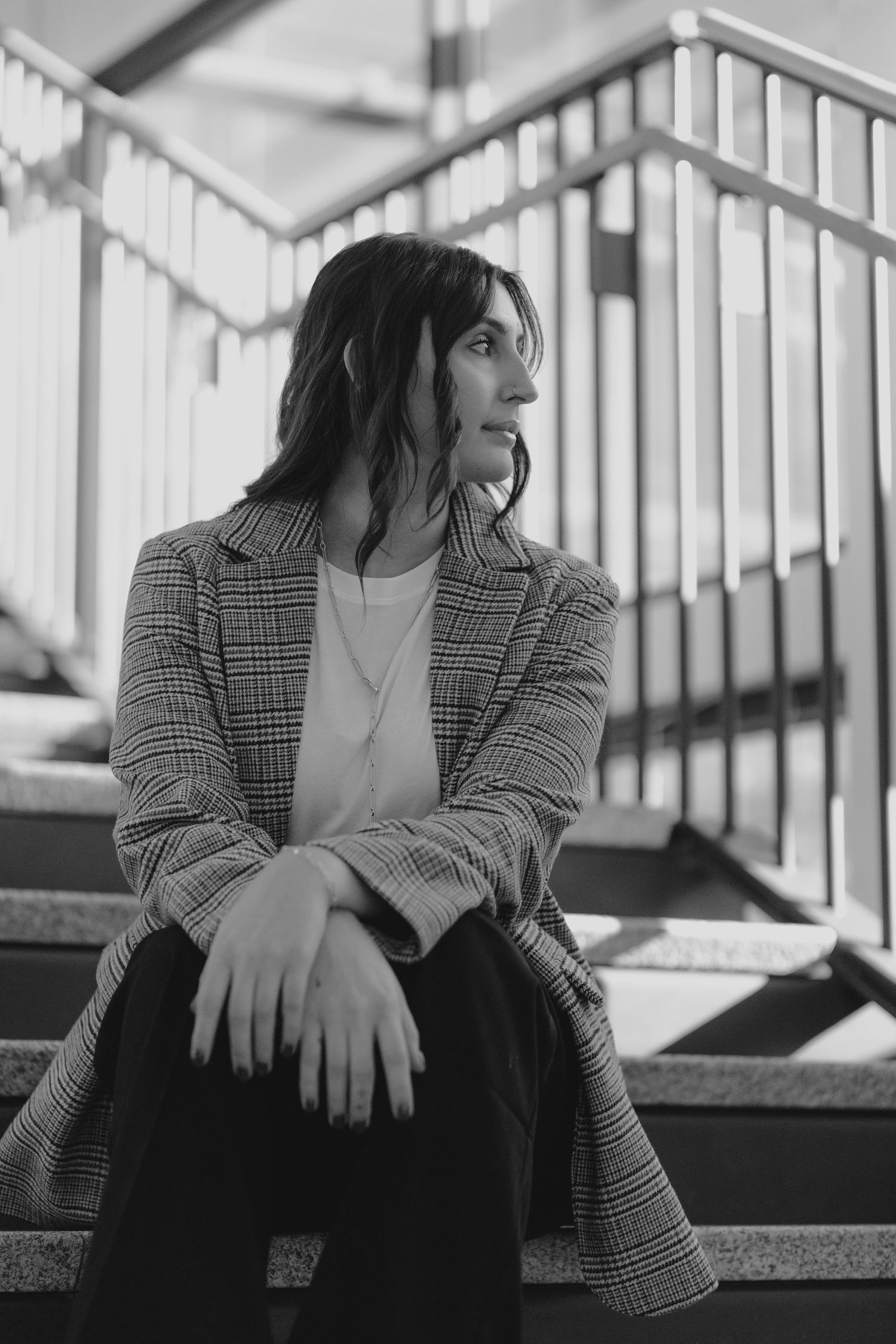Black and white portrait of someone in a plaid blazer sitting contemplatively on stairs.
