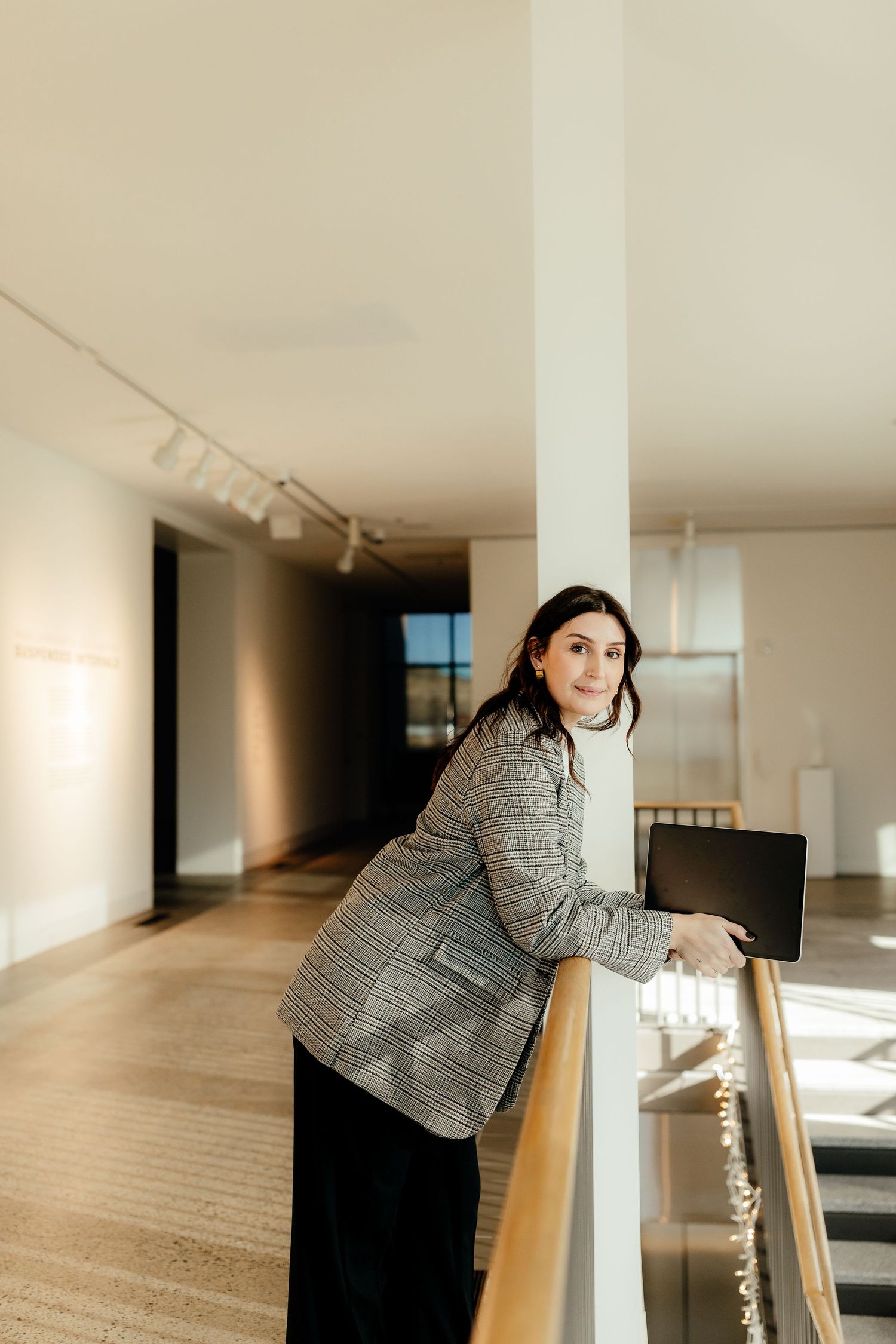 Someone in a plaid blazer stands by a railing in a modern indoor space with warm lighting.