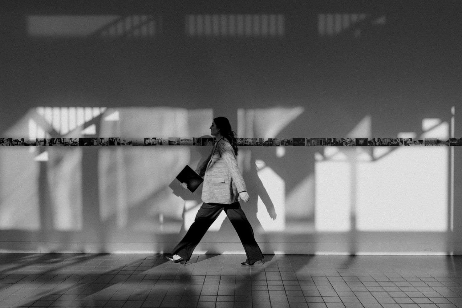 Blurred black and white motion shot of a person walking through a bright corridor carrying a guitar case.