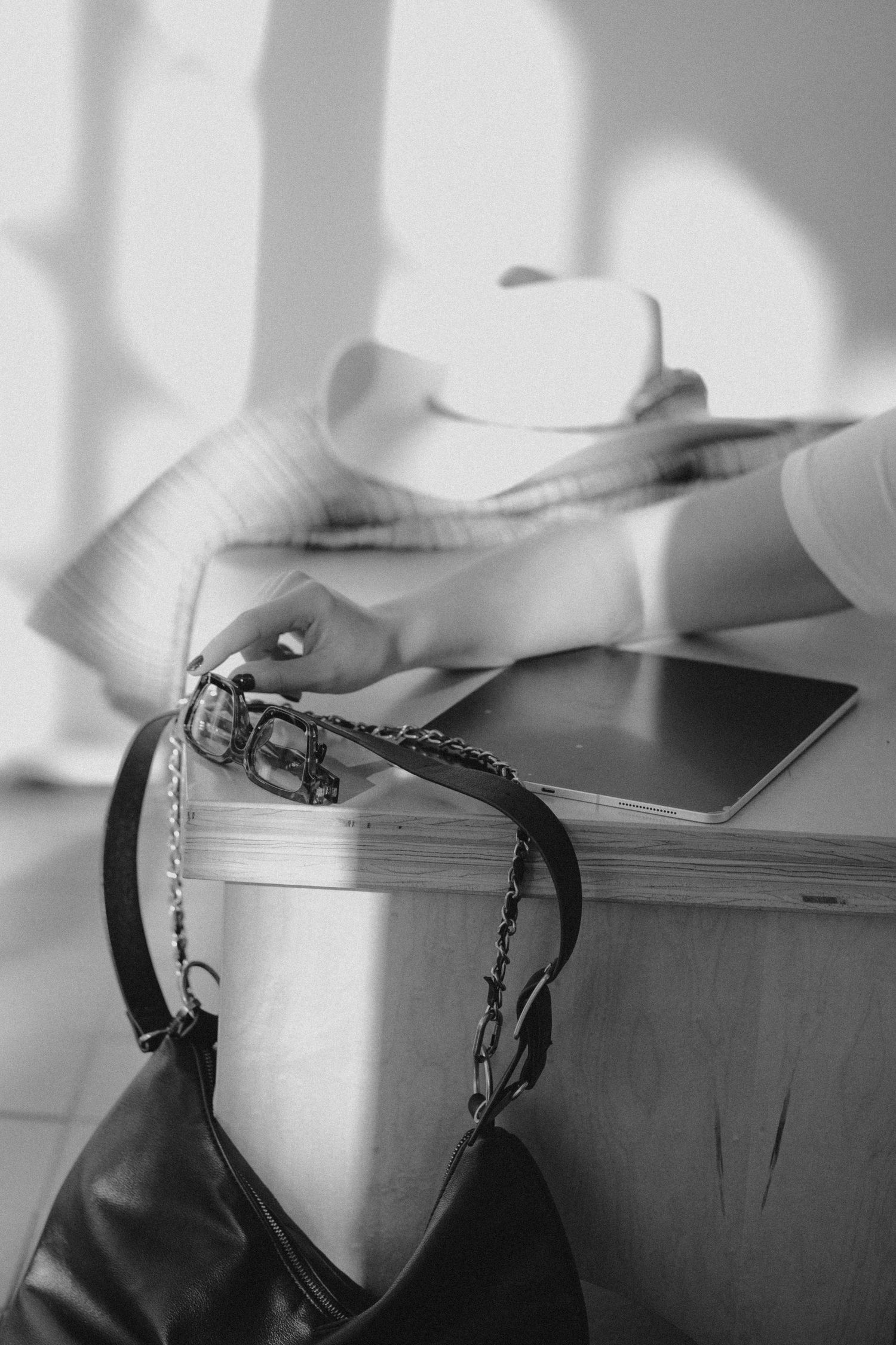 A black and white photograph showing a purse strap and coffee cup on a table casting dramatic shadows.
