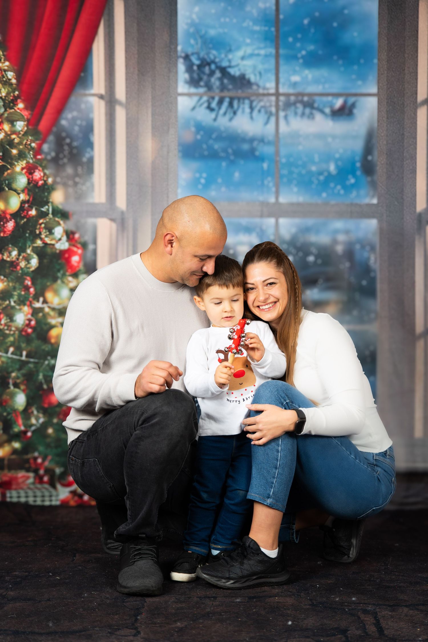 Family poses for Christmas photo by decorated tree and snowy window.