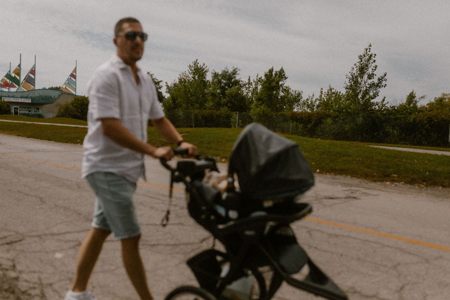 A person pushes a stroller along a paved path on a cloudy day with trees in the background.