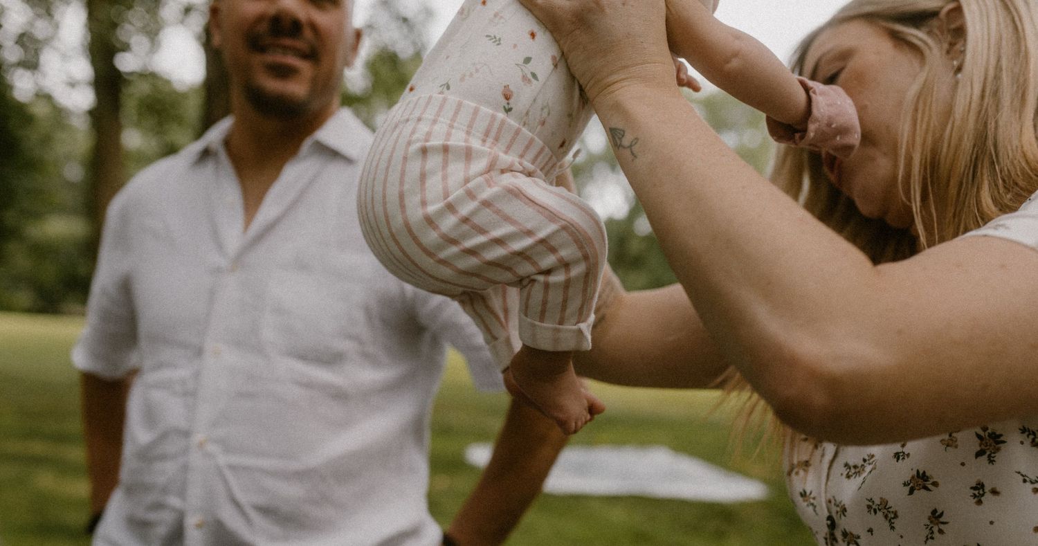 A tender family moment captured in a sunlit park setting with a small baby.