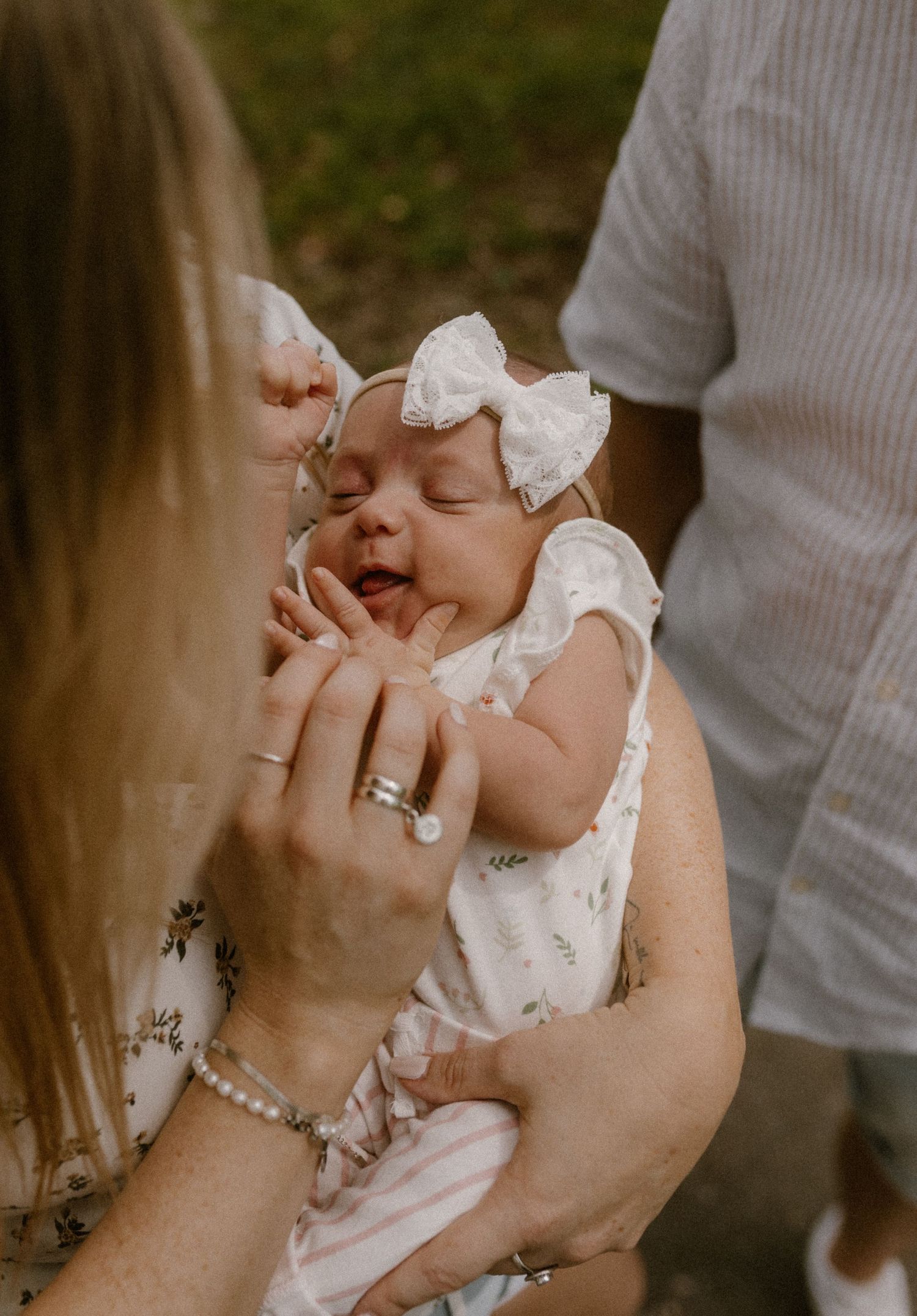A sweet moment with a baby wearing a white bow while being held outdoors.