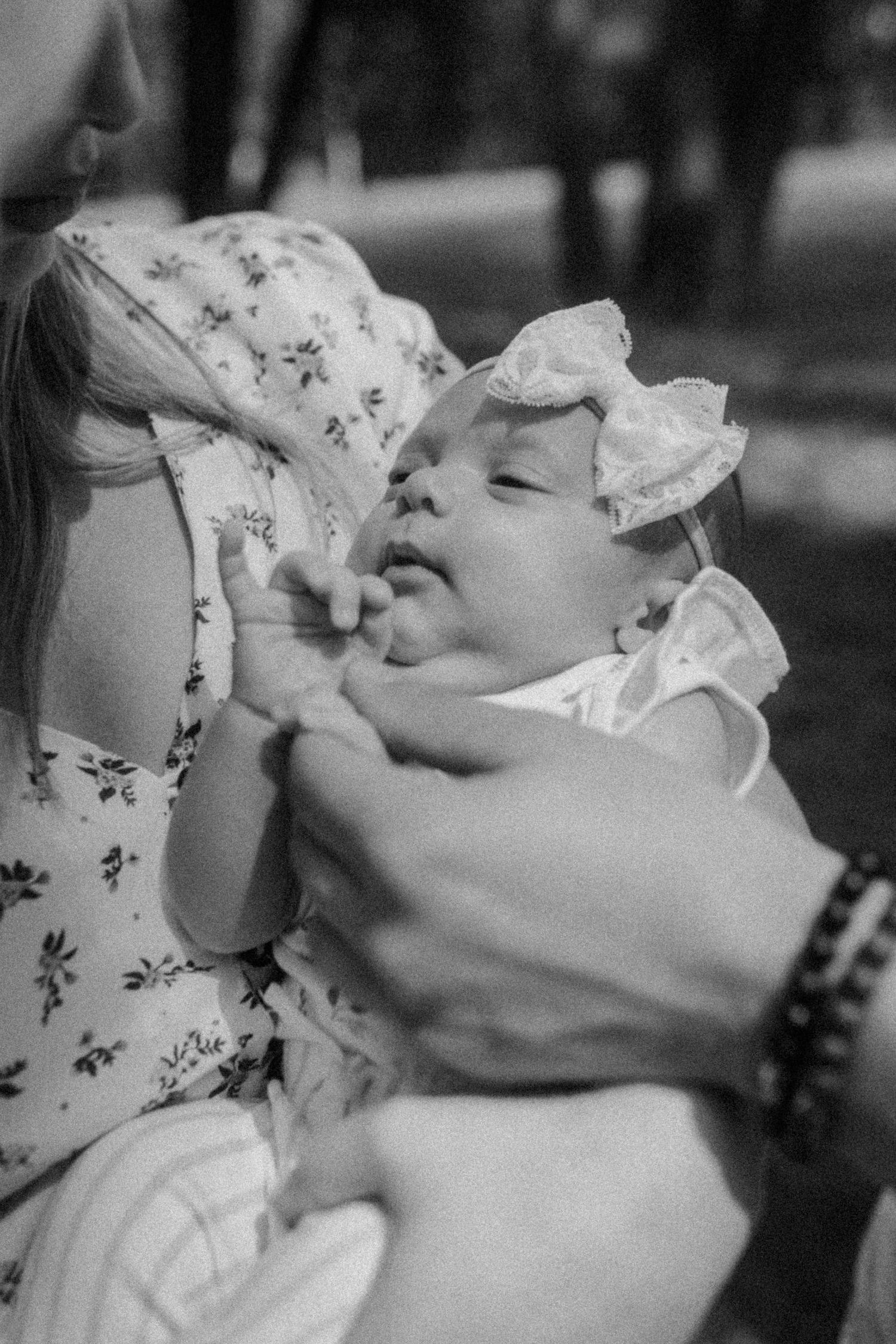 Black and white close-up of a baby being tenderly held outdoors.