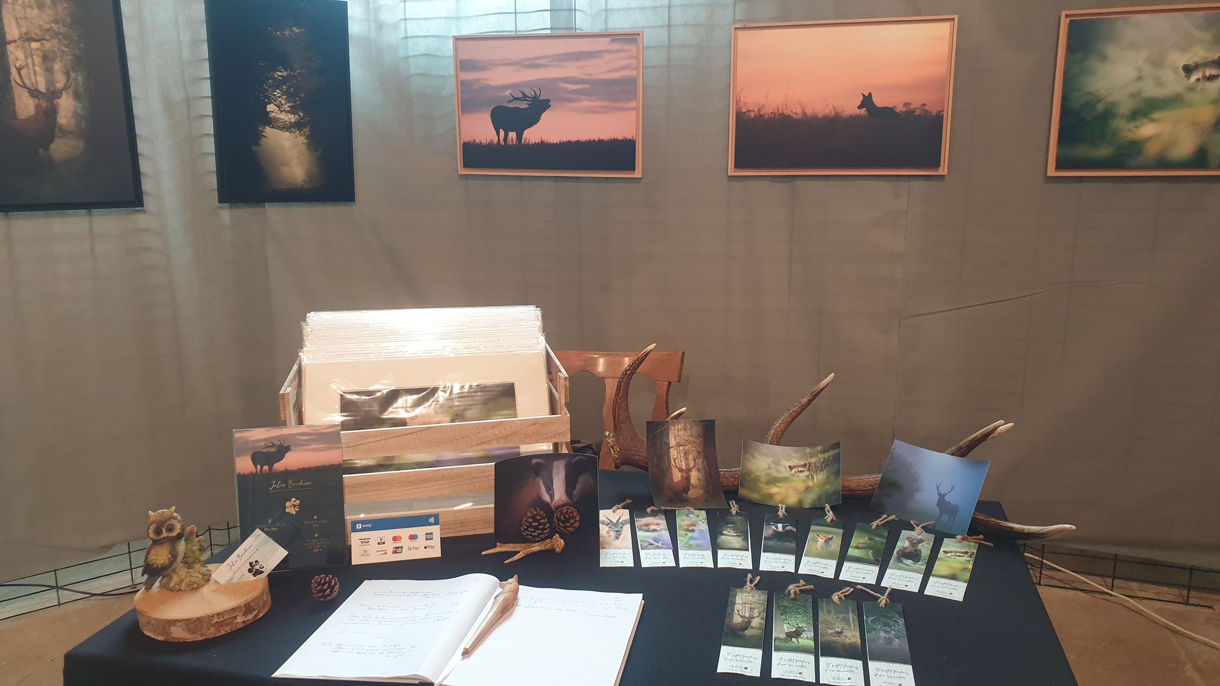 Photography display table with prints, materials and decorative elements against a wall with framed artwork.