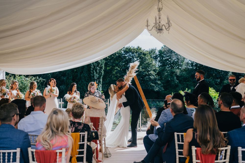 Newlyweds celebrate with guests during outdoor wedding ceremony under elegant white tent canopy with chandelier.