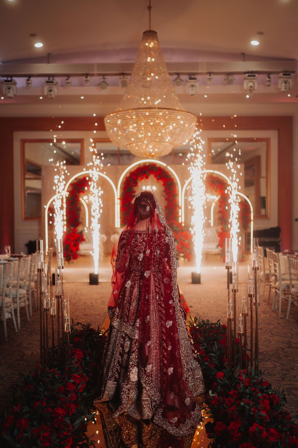 Dramatic wedding venue setup with crystal chandelier and illuminated arches lined with red roses.
