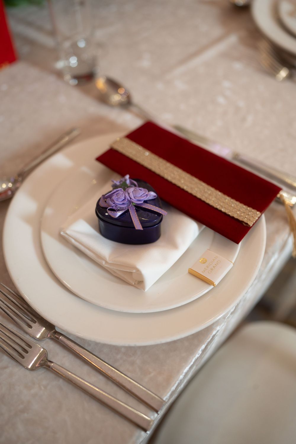 Elegant place setting with white plate, burgundy napkin and purple favor box.