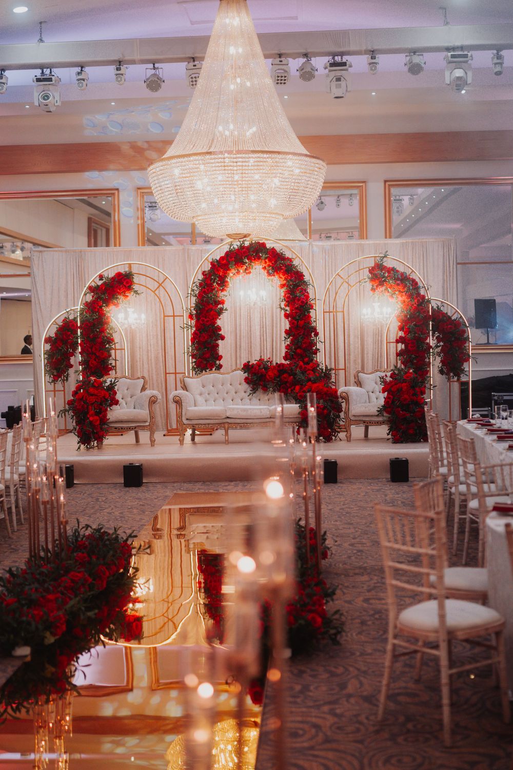 Luxurious wedding venue setup with crystal chandelier and red floral arches creating a romantic atmosphere.