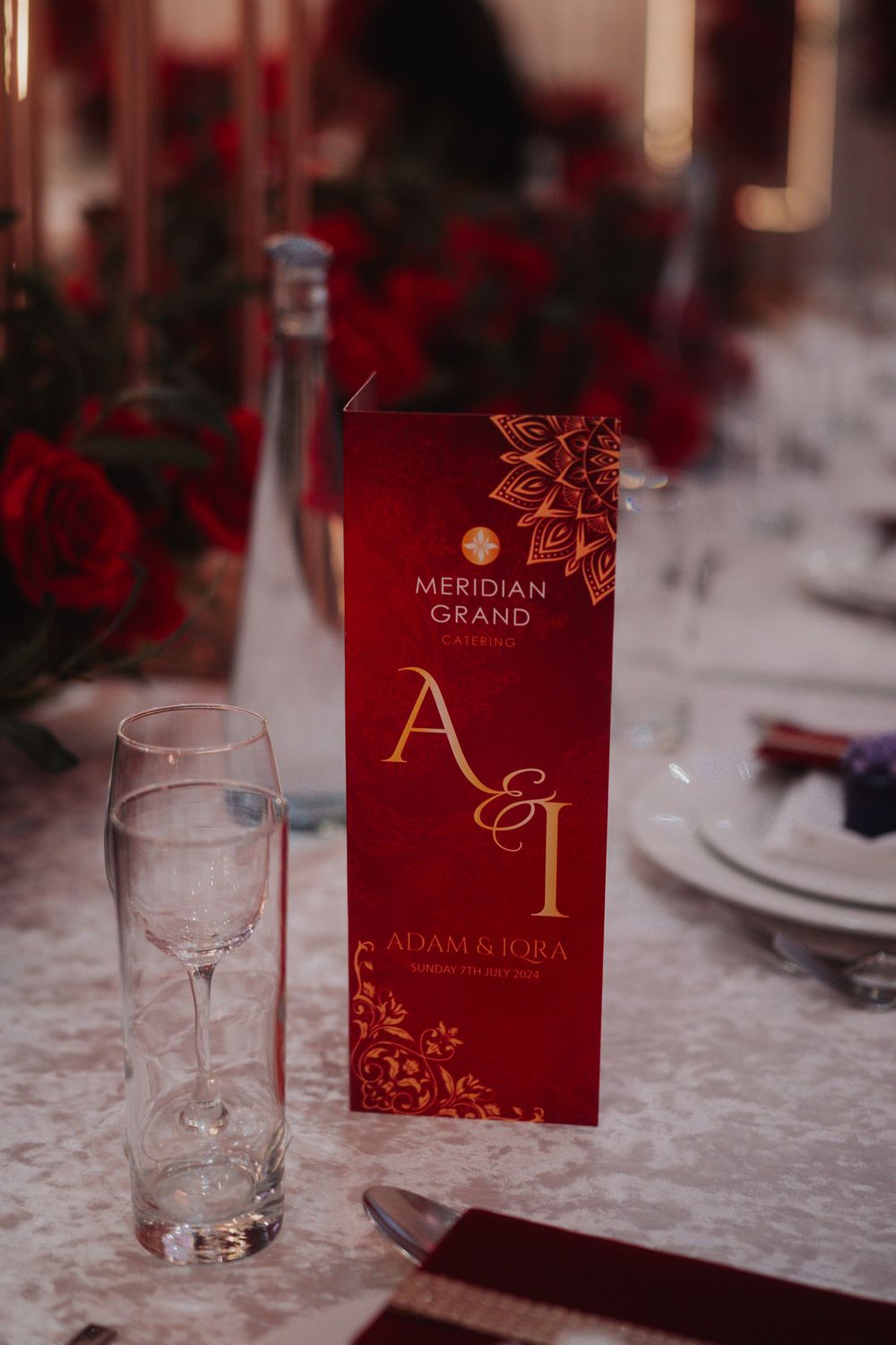 Red wedding menu card from Meridian Grand with elegant gold details next to empty wine glass.