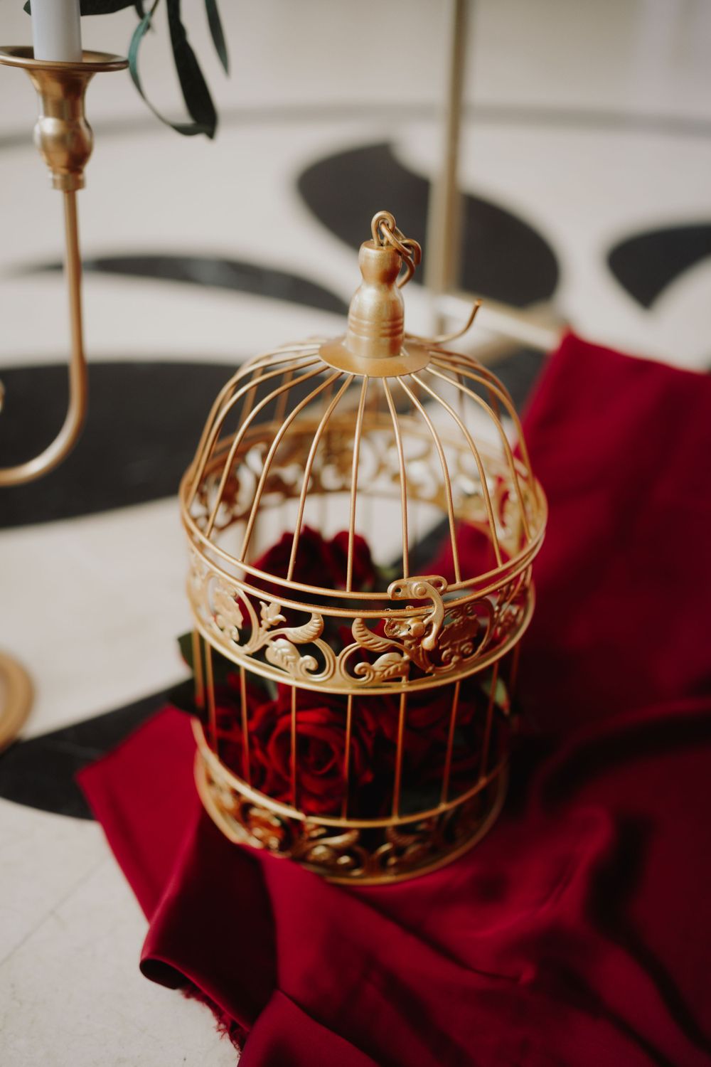 Decorative gold birdcage filled with red roses on white and black surface.