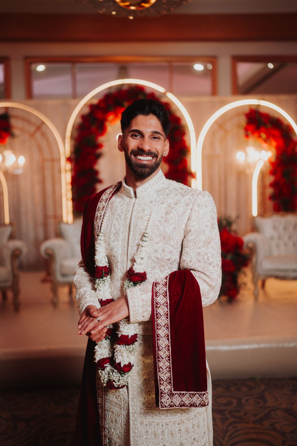 Formal wedding portrait in front of illuminated arches decorated with red roses.