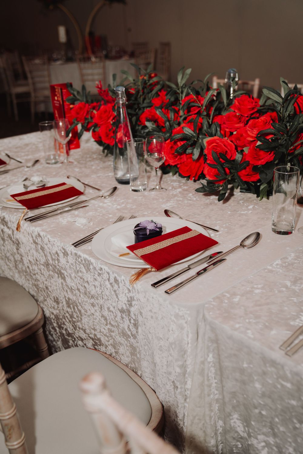 Elegant wedding table setting with red flowers, white lace tablecloth, and formal place settings.