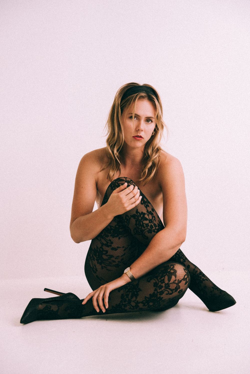 Artistic portrait of model wearing black lace outfit in minimalist studio setting.