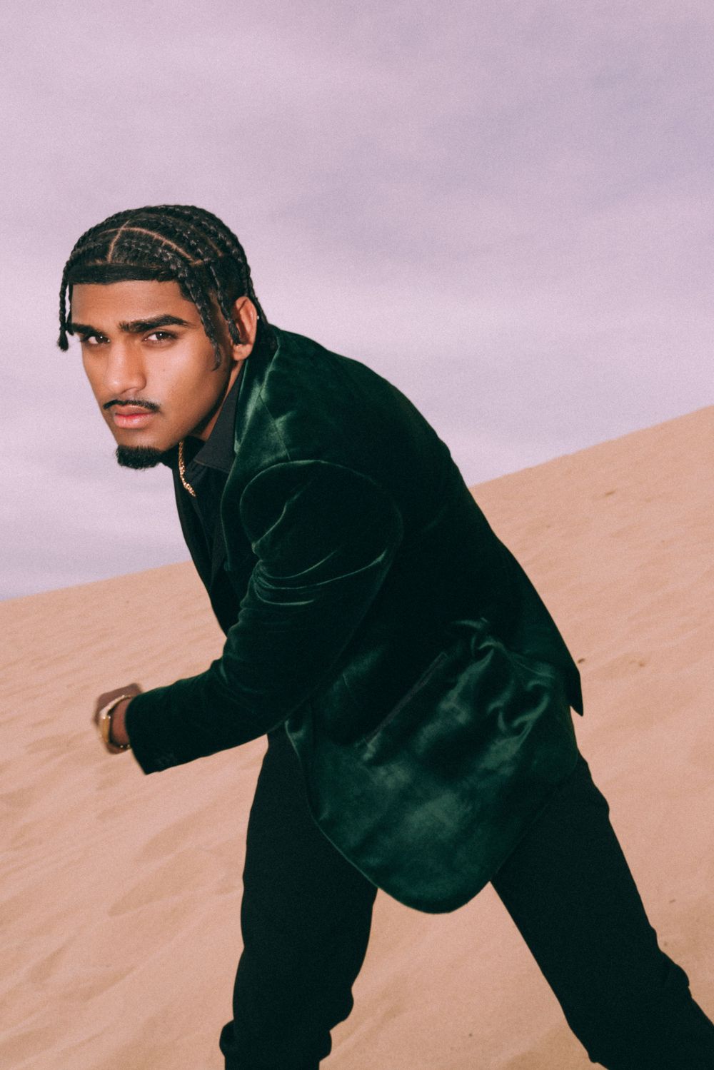 Portrait of model in dark velvet jacket posing against desert backdrop.