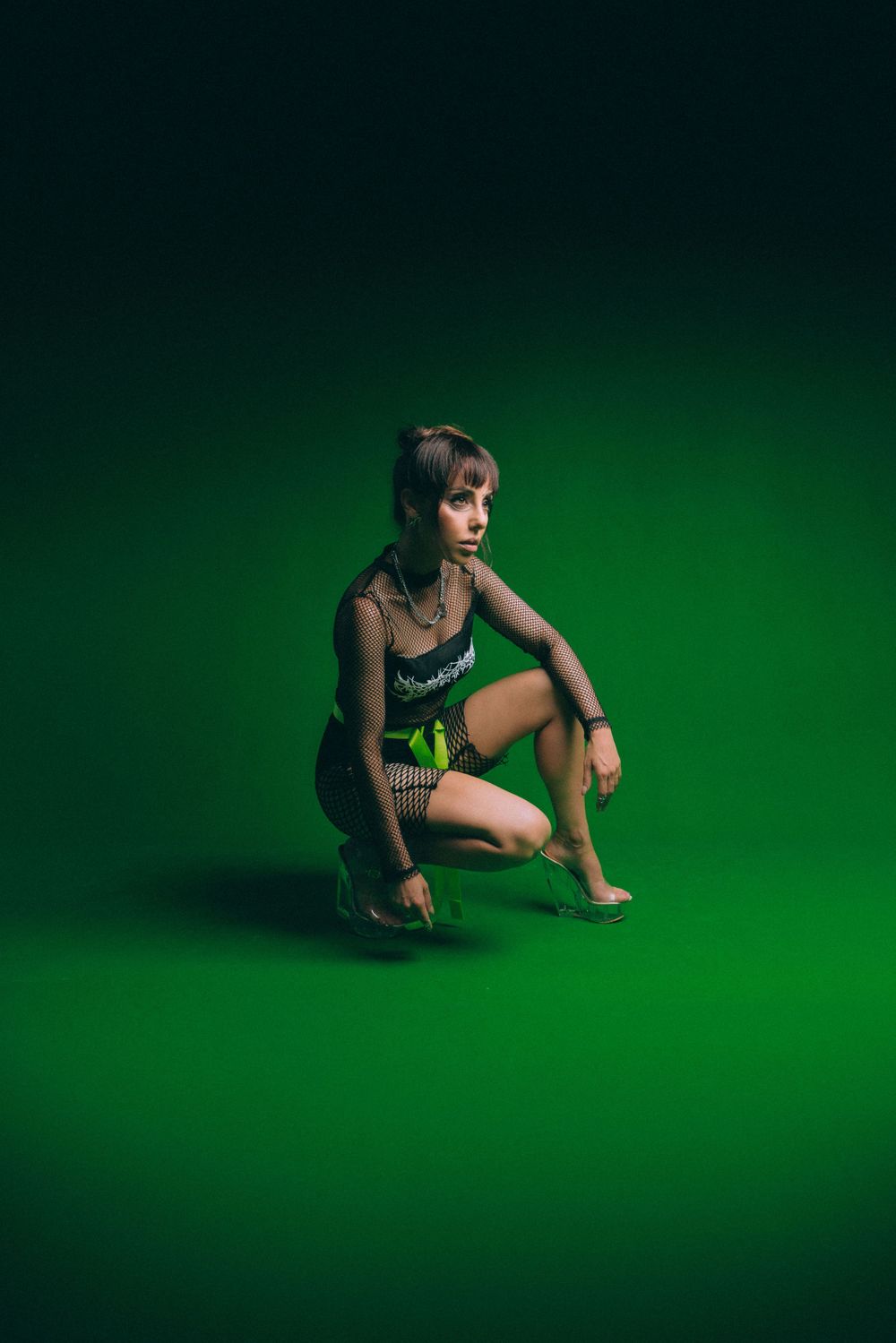 Artistic portrait on green background with model in mesh outfit striking dynamic pose.