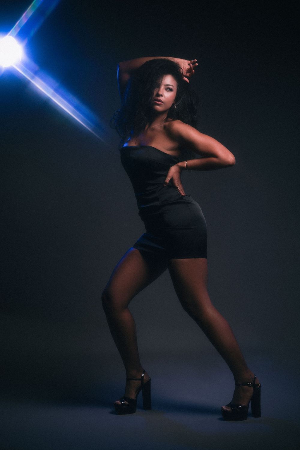Dancer in black dress striking dynamic pose with dramatic blue lighting effect.
