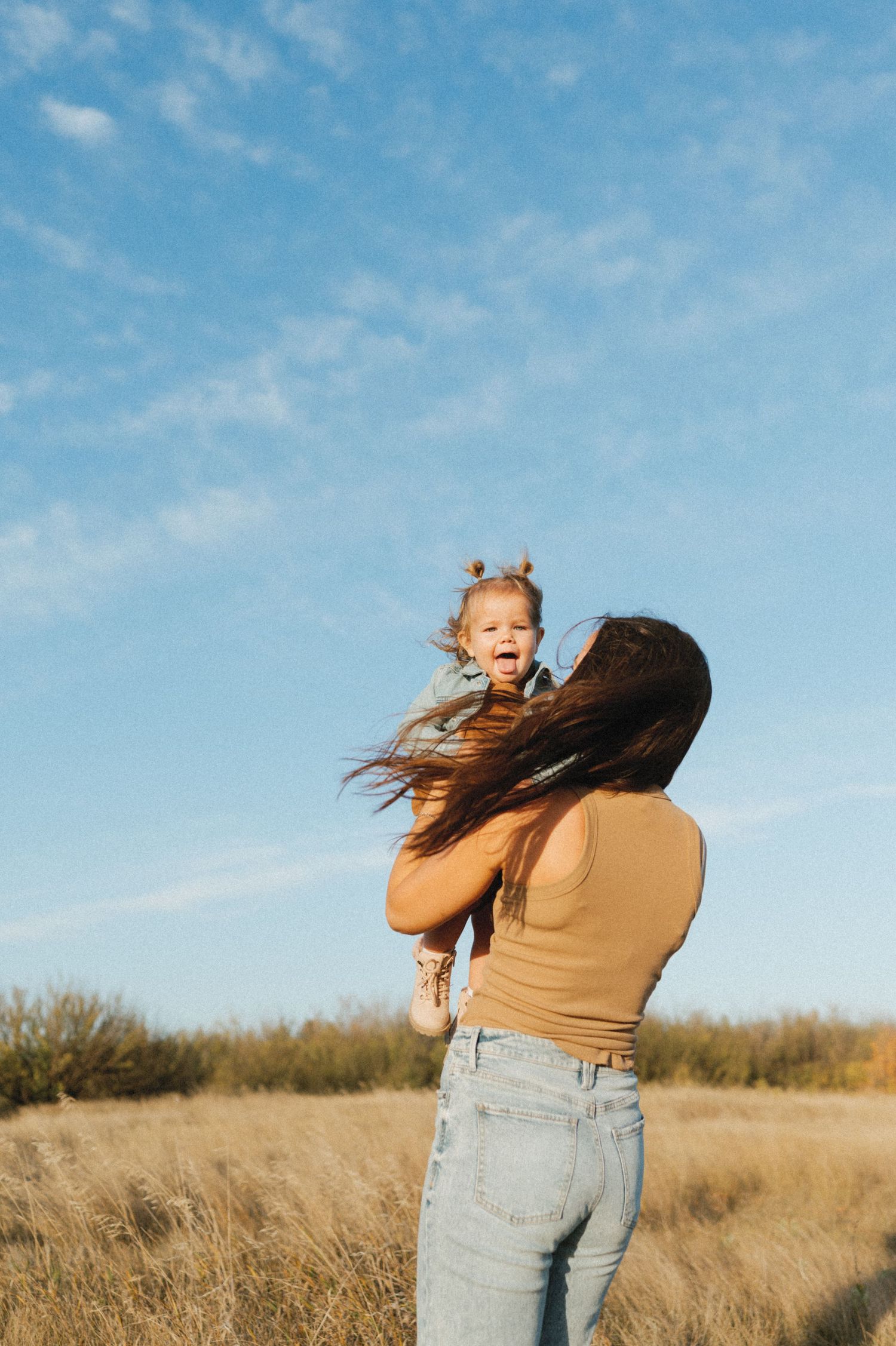 Parent lifting small child in golden field against bright blue sky.