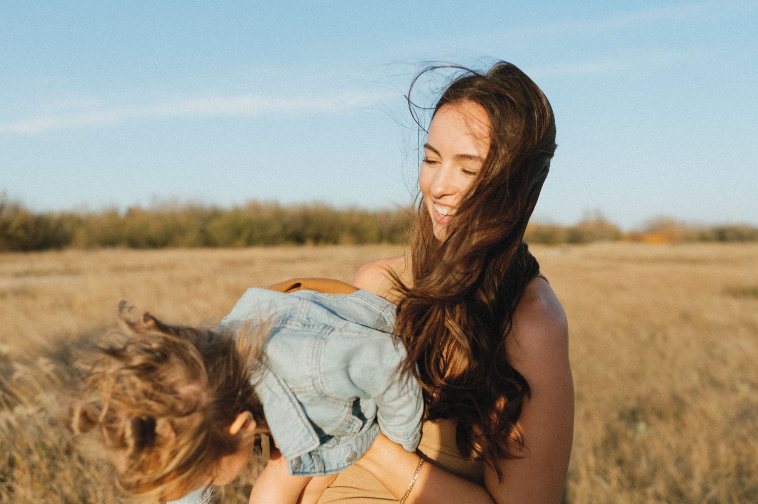 Woman with flowing hair stands in golden field during sunset with wind blowing through her hair.