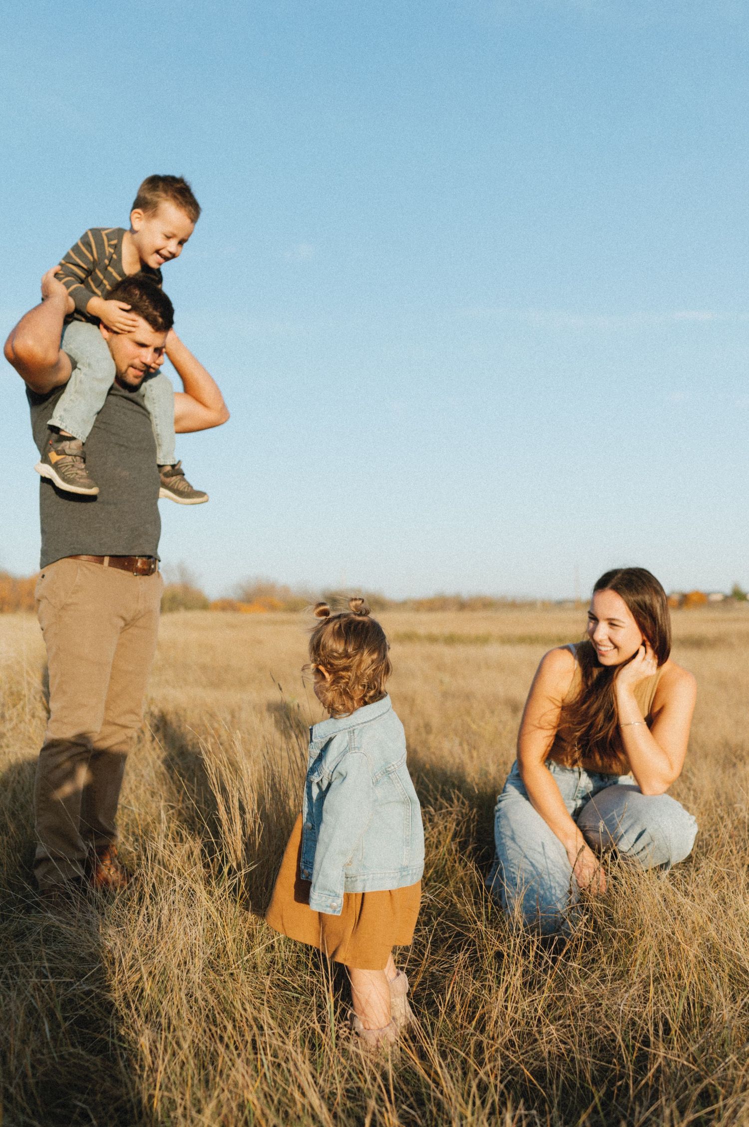 Family enjoying outdoor time together in tall grass field during golden hour.