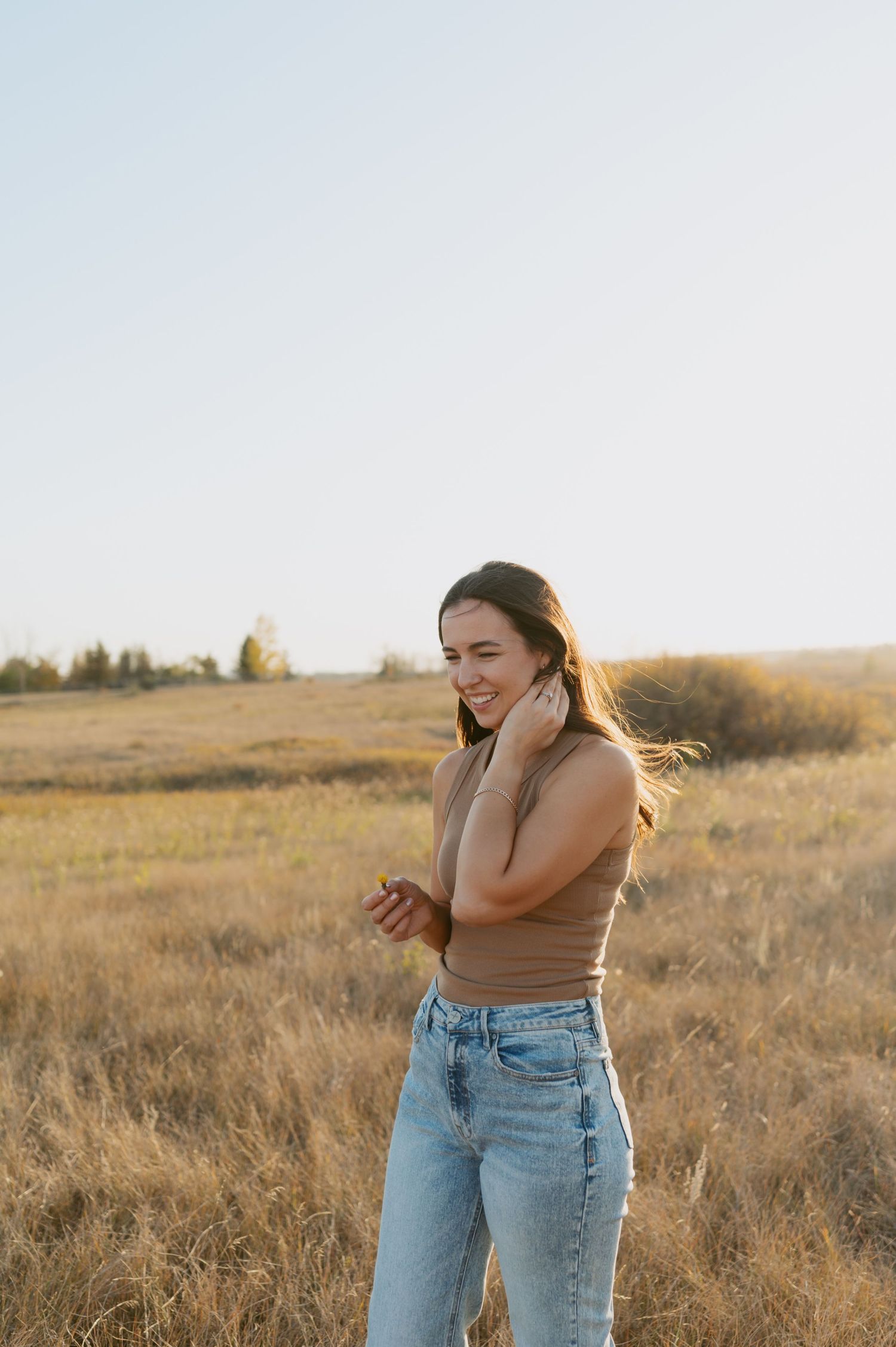 Person in casual outfit smiles and laughs while standing in dry autumn field.