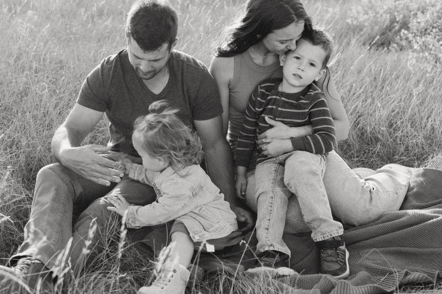 Black and white portrait of family sitting together on blanket outdoors.