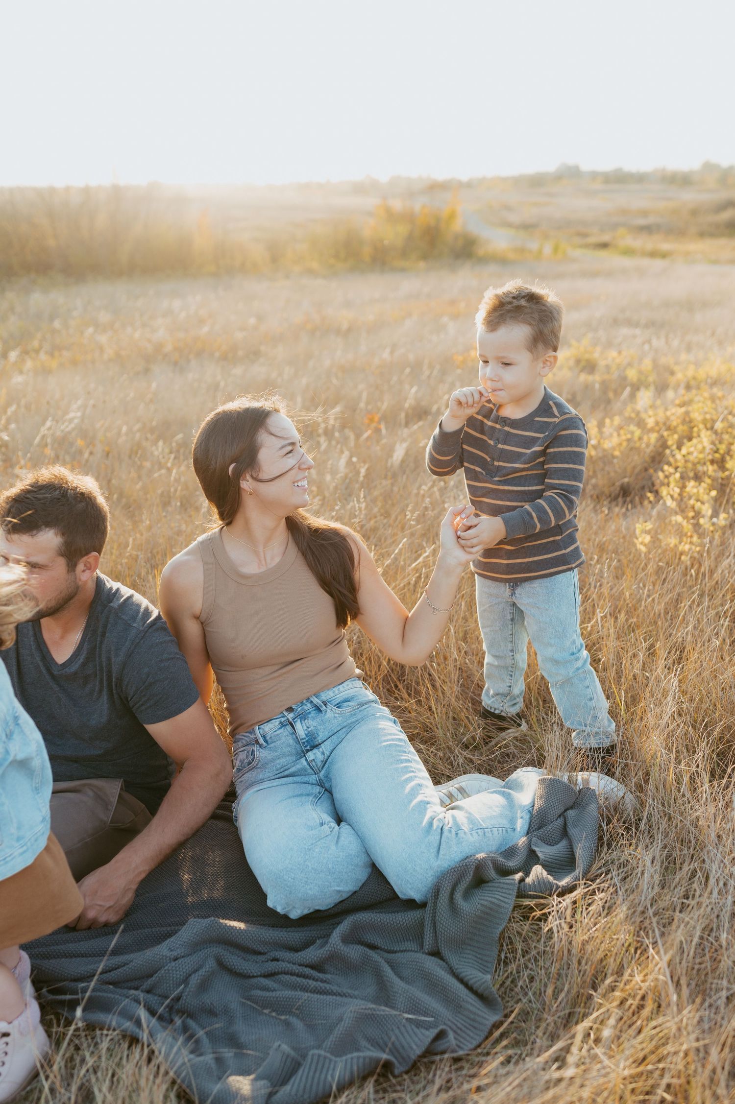Family relaxing on blanket in autumn field during golden hour sunset.