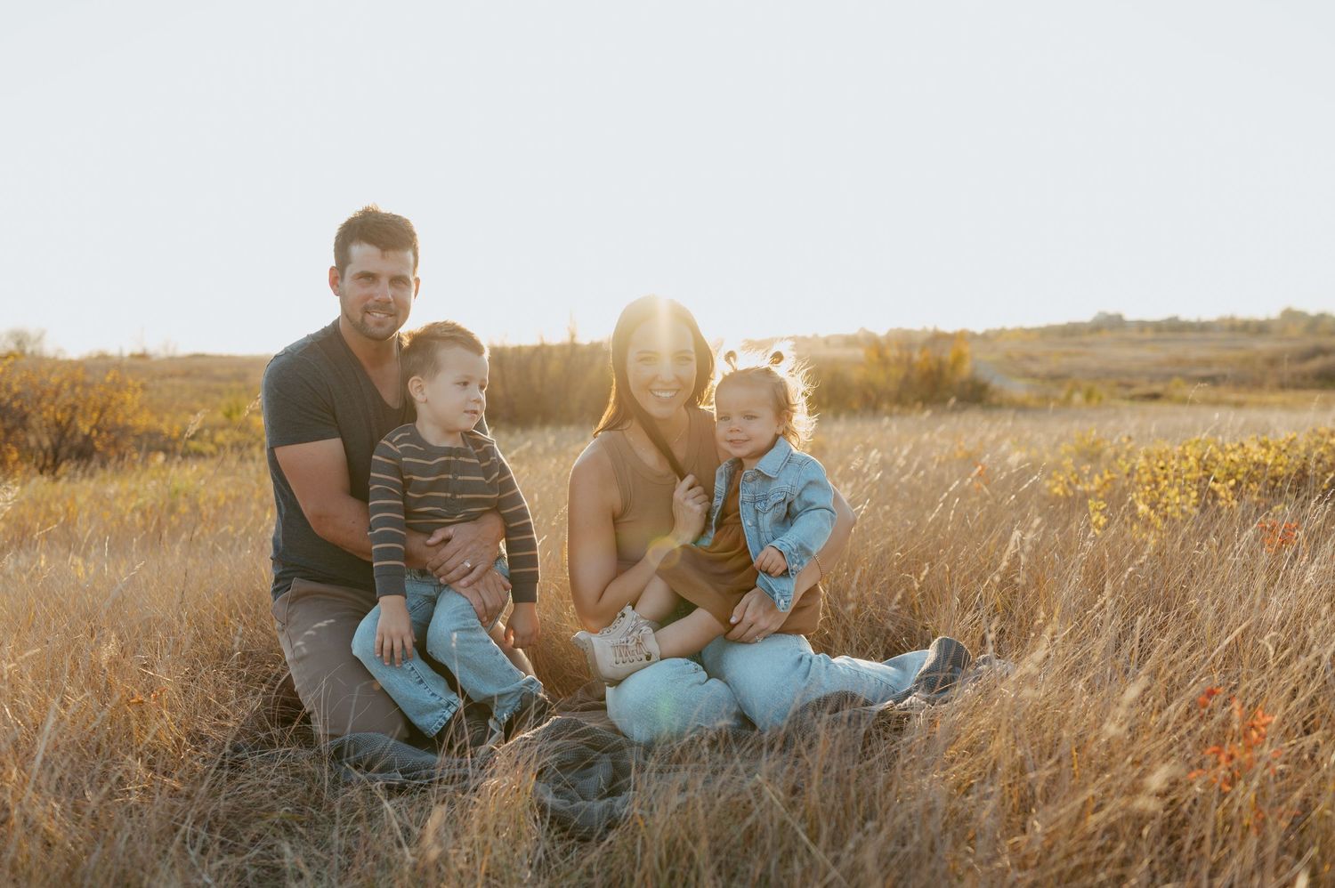 Family sitting together in golden field during sunset photoshoot.