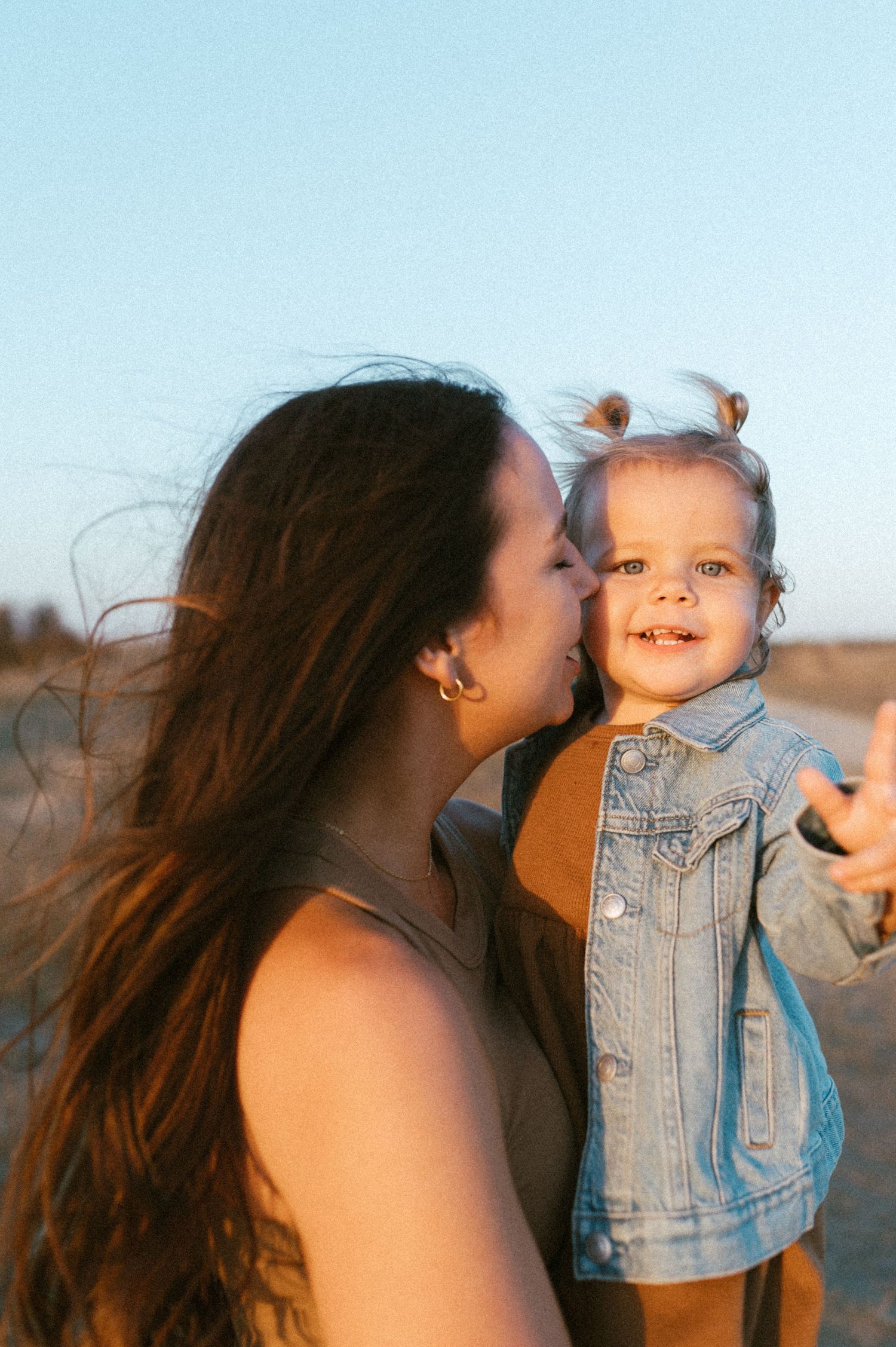 Sweet candid moment between parent and small child in denim jacket during golden hour.