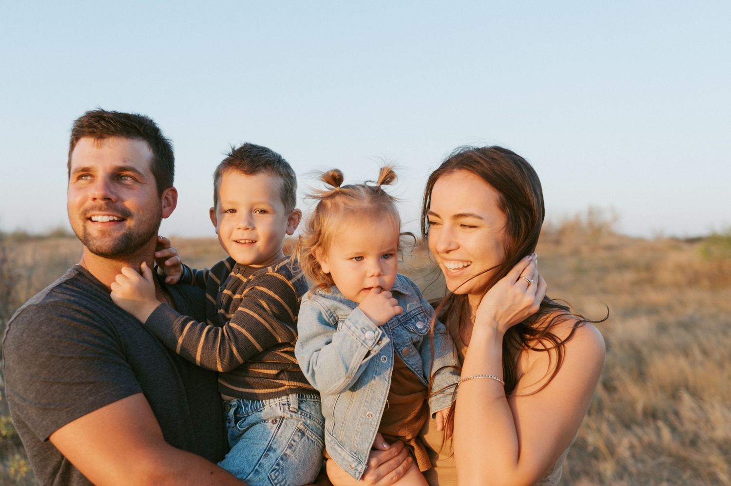 Happy family portrait of four people smiling outdoors during golden hour.